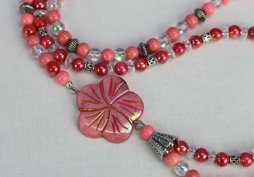 Double strand asymmetrical necklace with shell flower focal, shell and glass beads in shades of pink, coral, and clear, silver plated beads, toggle clasp